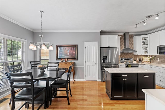 kitchen with wall chimney range hood, dark cabinets, light wood-style flooring, a center island, and stainless steel appliances