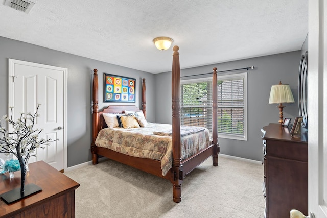 bedroom with baseboards, light colored carpet, a textured ceiling, and visible vents
