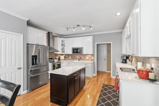 kitchen featuring a sink, appliances with stainless steel finishes, wall chimney exhaust hood, and white cabinetry