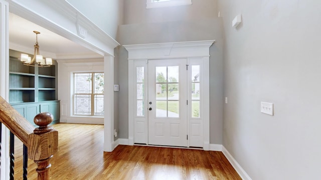 entryway featuring wood finished floors, ornamental molding, baseboards, a high ceiling, and a notable chandelier