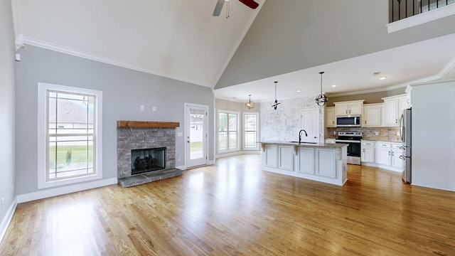 unfurnished living room featuring a ceiling fan, a stone fireplace, a sink, high vaulted ceiling, and light wood-style floors