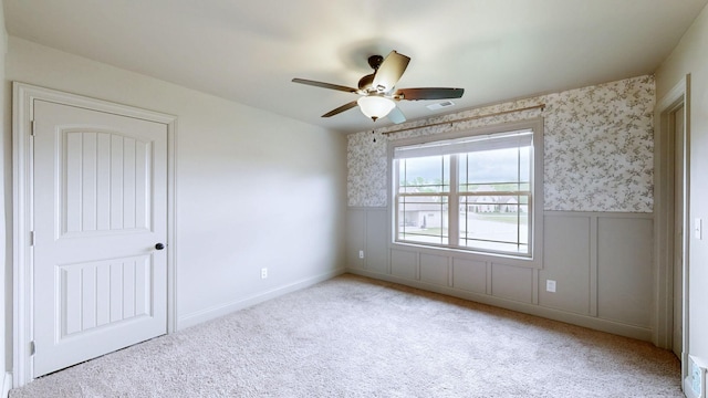empty room with a wainscoted wall, visible vents, ceiling fan, carpet floors, and wallpapered walls