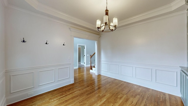 unfurnished dining area featuring ornamental molding, an inviting chandelier, a decorative wall, a wainscoted wall, and light wood-type flooring
