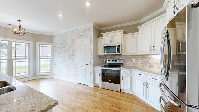 kitchen featuring light stone counters, ornamental molding, an inviting chandelier, backsplash, and stainless steel appliances