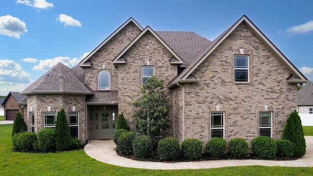 view of front of house featuring a shingled roof, brick siding, and a front yard