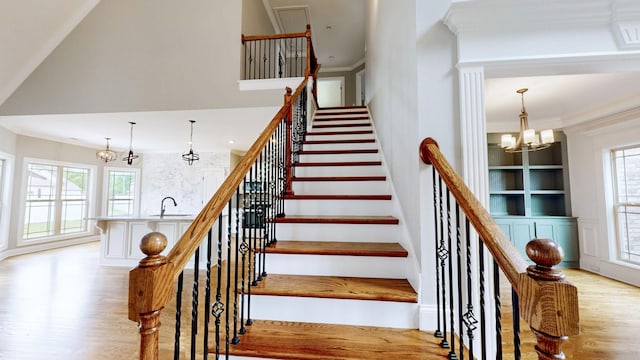 staircase with crown molding, plenty of natural light, wood finished floors, and a notable chandelier