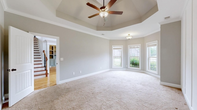 empty room with a ceiling fan, a tray ceiling, carpet, baseboards, and visible vents