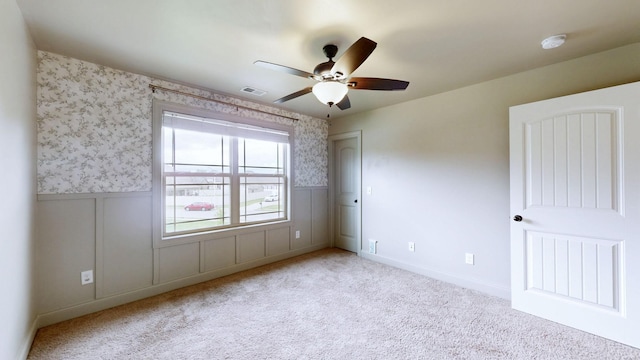 spare room with carpet flooring, visible vents, wainscoting, and ceiling fan