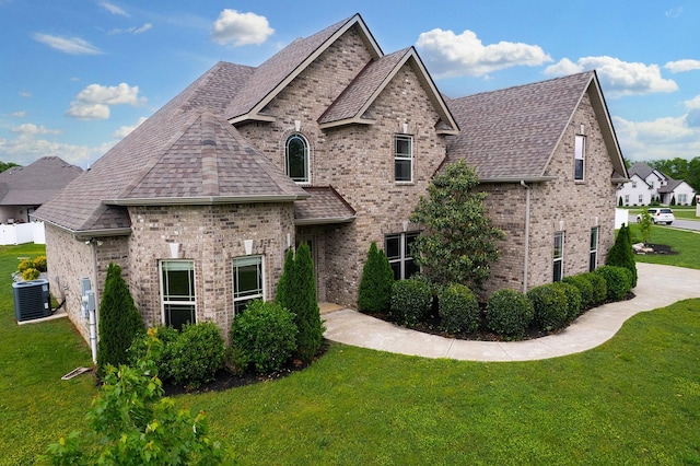 french provincial home with a shingled roof, a front lawn, cooling unit, and brick siding