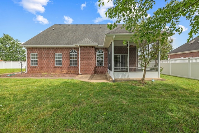 rear view of property with roof with shingles, brick siding, a sunroom, a fenced backyard, and a yard