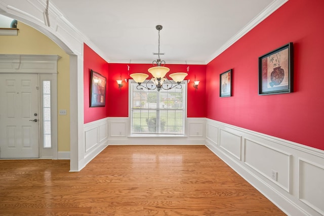 unfurnished dining area featuring crown molding, a notable chandelier, a wainscoted wall, and light wood-type flooring