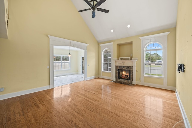 unfurnished living room with a ceiling fan, a fireplace with flush hearth, wood finished floors, high vaulted ceiling, and baseboards