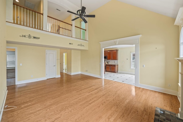 unfurnished living room with high vaulted ceiling, baseboards, a ceiling fan, and light wood-style flooring