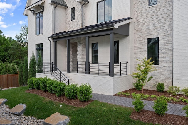view of home's exterior featuring covered porch, brick siding, and fence