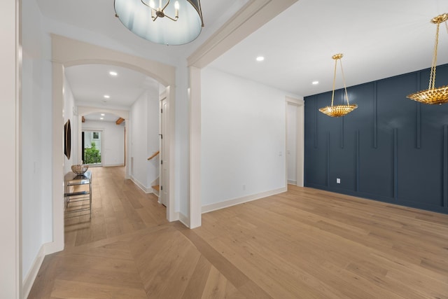 foyer entrance with arched walkways, baseboards, a chandelier, light wood-style floors, and stairway