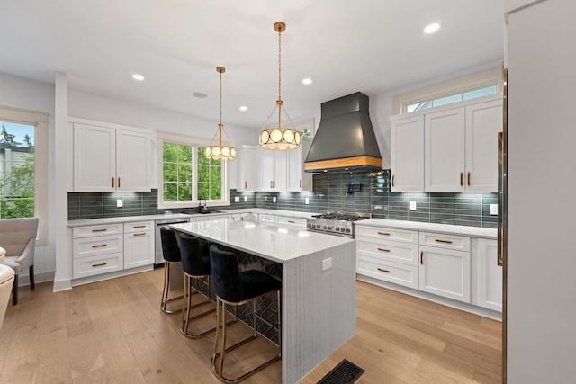 kitchen featuring premium range hood, stainless steel appliances, a sink, white cabinets, and a breakfast bar area