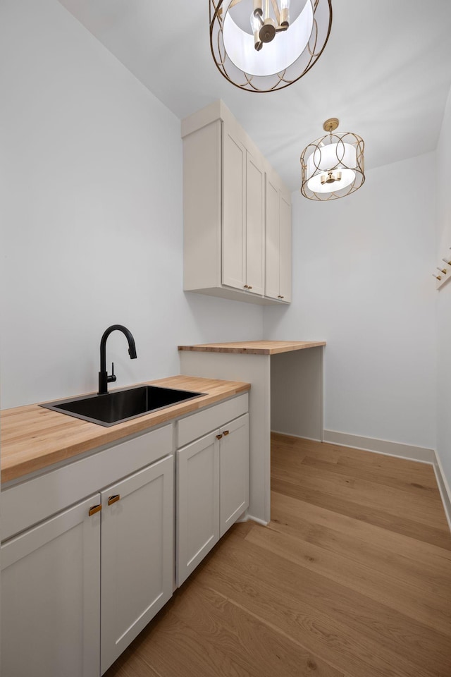 laundry room featuring light wood-style flooring, baseboards, a sink, and a chandelier