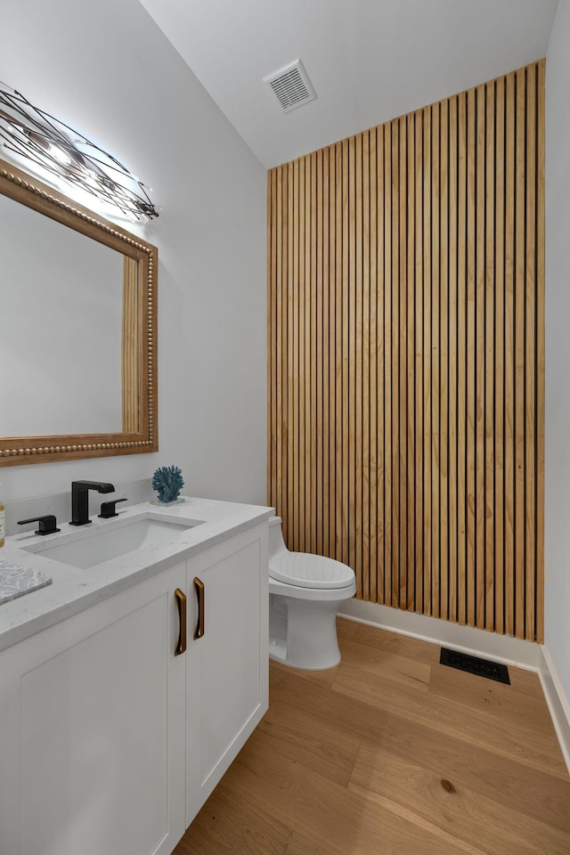 half bath with wood finished floors, toilet, vanity, and lofted ceiling