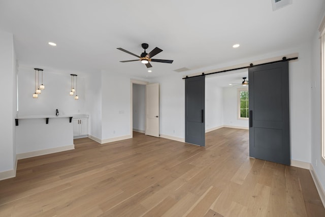 unfurnished living room with a barn door, ceiling fan, light wood-type flooring, and recessed lighting