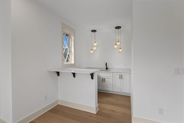 bar area with a sink, light wood-style flooring, pendant lighting, and baseboards