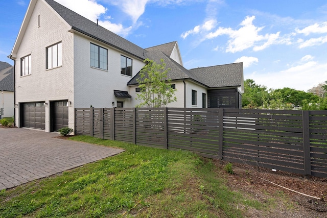 view of side of home featuring an attached garage, fence, decorative driveway, and brick siding