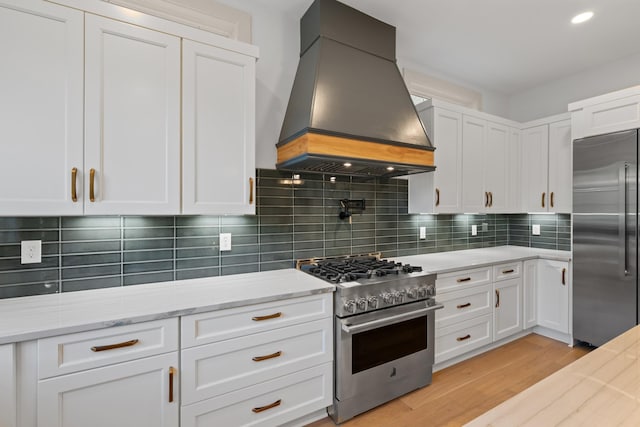 kitchen with high end appliances, premium range hood, white cabinets, light wood-style floors, and light stone counters