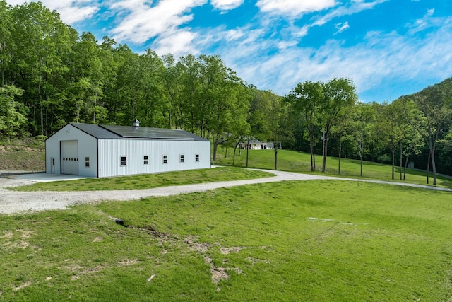 view of property's community with a detached garage, a view of trees, an outdoor structure, gravel driveway, and a yard