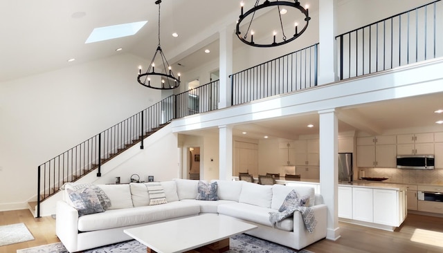 living area featuring stairs, wood finished floors, high vaulted ceiling, a chandelier, and a skylight