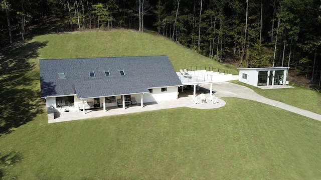 rear view of property featuring a lawn, a shingled roof, and a patio area
