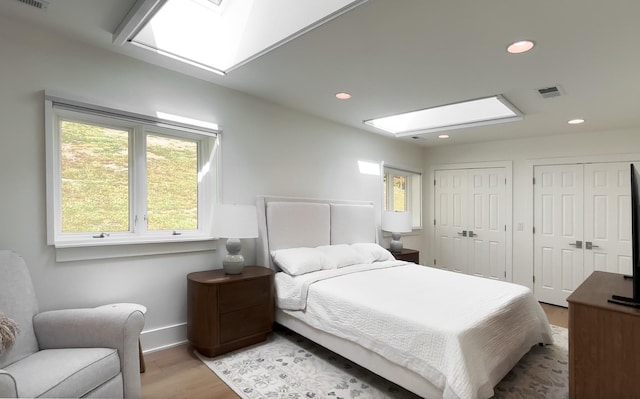 bedroom with a skylight, visible vents, multiple windows, and wood finished floors