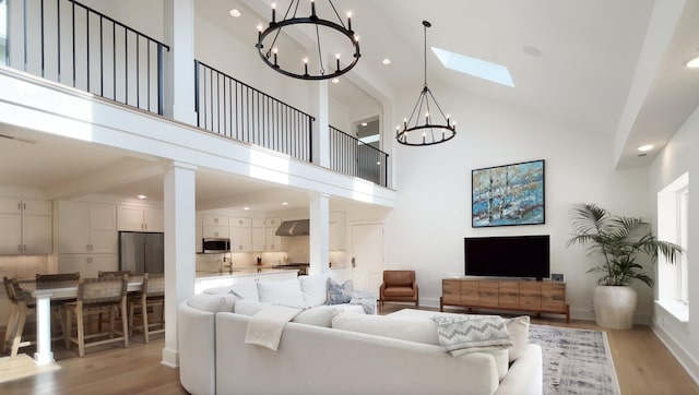 living room with a skylight, a chandelier, light wood finished floors, and high vaulted ceiling