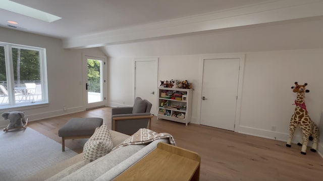 living area with baseboards, wood finished floors, and vaulted ceiling with skylight