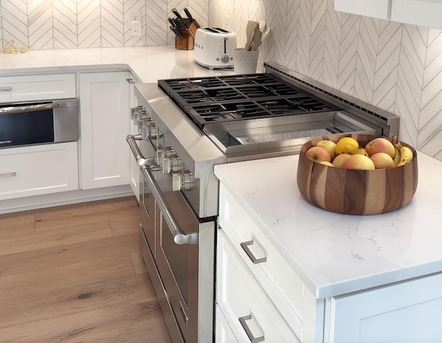 kitchen featuring high end stove, light stone countertops, light wood-type flooring, a warming drawer, and white cabinetry