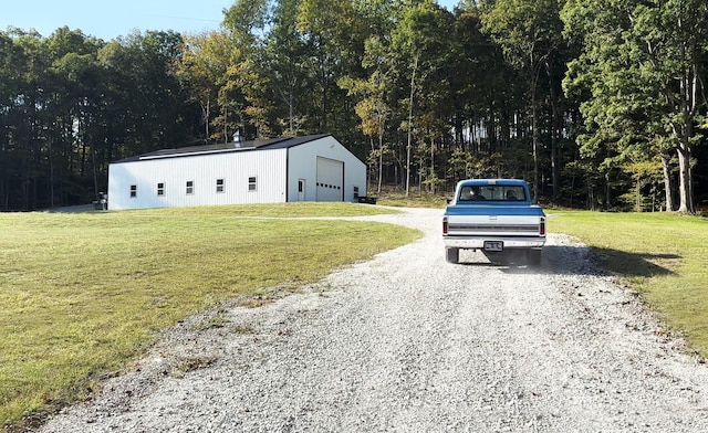 exterior space with a lawn, a view of trees, and gravel driveway