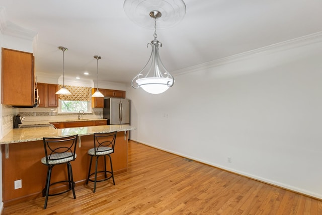 kitchen with brown cabinets, a sink, freestanding refrigerator, a peninsula, and ornamental molding