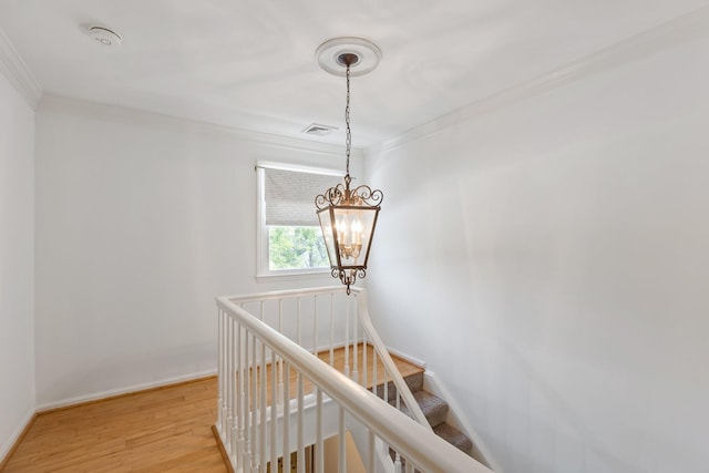 stairs with a notable chandelier, baseboards, wood finished floors, visible vents, and ornamental molding