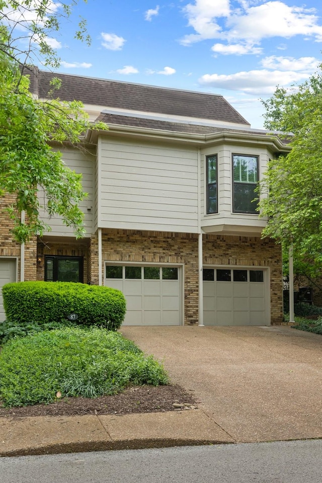 exterior space featuring a garage, a shingled roof, driveway, and brick siding