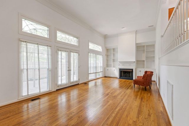 unfurnished living room with visible vents, ornamental molding, a fireplace, built in shelves, and light wood finished floors