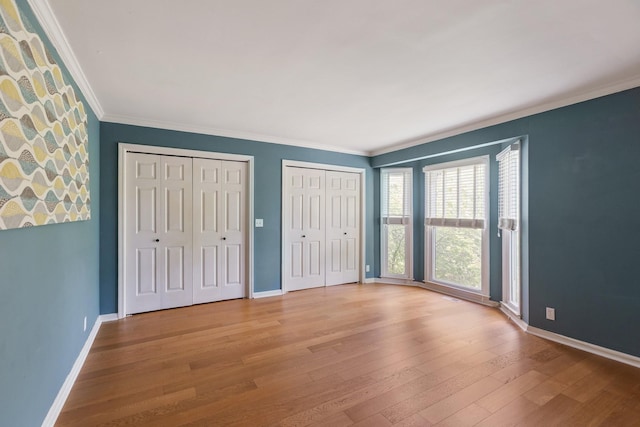 unfurnished bedroom with baseboards, ornamental molding, multiple closets, and wood finished floors