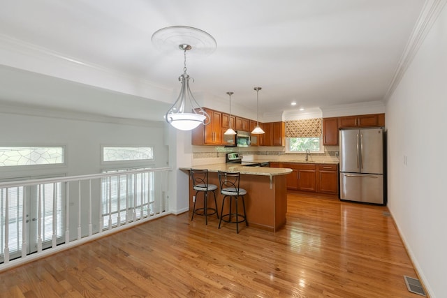 kitchen featuring appliances with stainless steel finishes, tasteful backsplash, light wood-type flooring, brown cabinets, and a sink