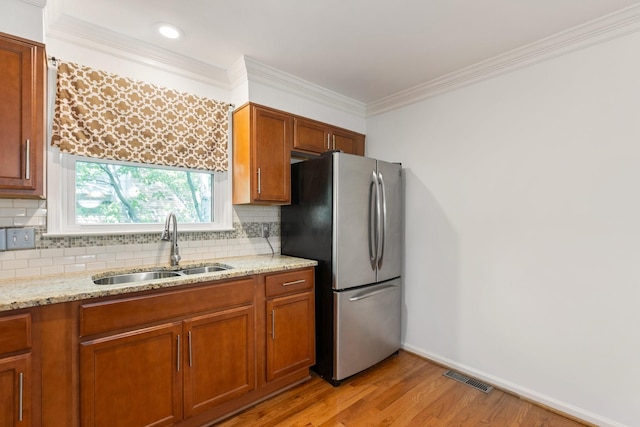 kitchen with a sink, freestanding refrigerator, decorative backsplash, light wood-type flooring, and visible vents