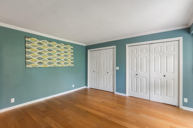 unfurnished bedroom with baseboards, ornamental molding, two closets, and wood finished floors