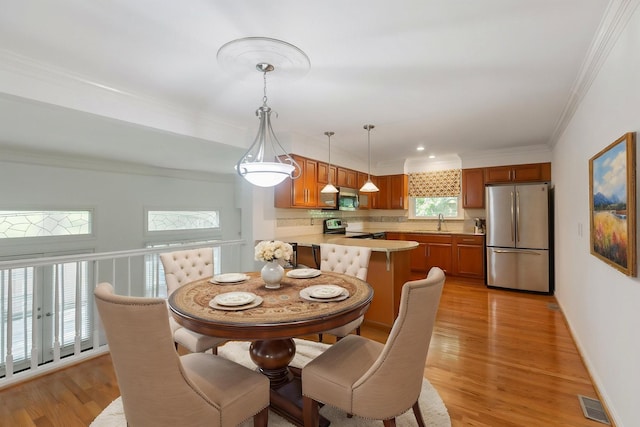 dining space featuring baseboards, ornamental molding, light wood-style flooring, and visible vents