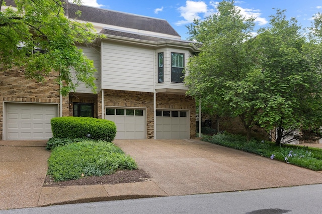 view of property featuring a garage, a shingled roof, driveway, and brick siding