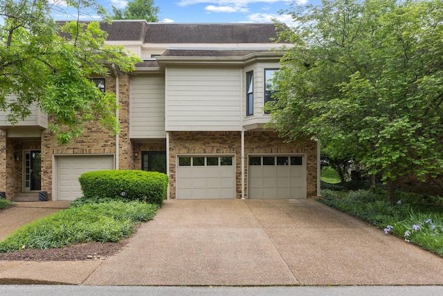 townhome / multi-family property with a garage, driveway, roof with shingles, and brick siding