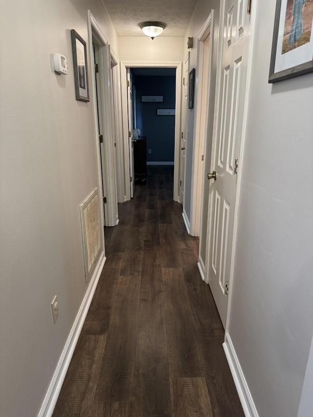 hallway featuring baseboards, visible vents, and dark wood finished floors