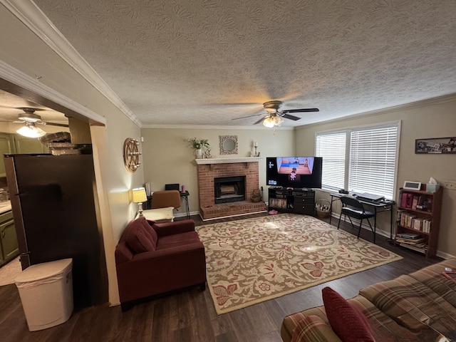 living area with ceiling fan, a textured ceiling, a brick fireplace, wood finished floors, and ornamental molding