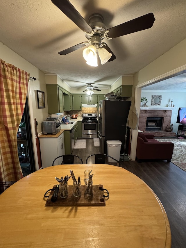 dining room with ceiling fan, a textured ceiling, a brick fireplace, a toaster, and dark wood-style floors
