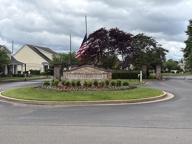 community / neighborhood sign with curved driveway, fence, and a gate