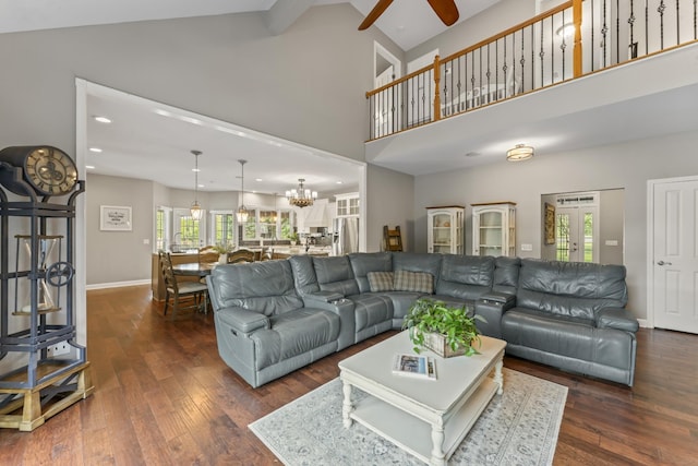 living area featuring high vaulted ceiling, baseboards, ceiling fan with notable chandelier, and dark wood-style flooring